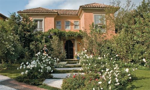 a house with white flowers in front of it and bushes around the entrance to the building