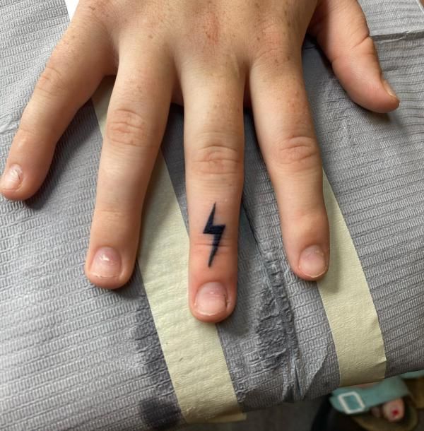 a person's hand with a lightning tattoo on their left thumb and the middle finger