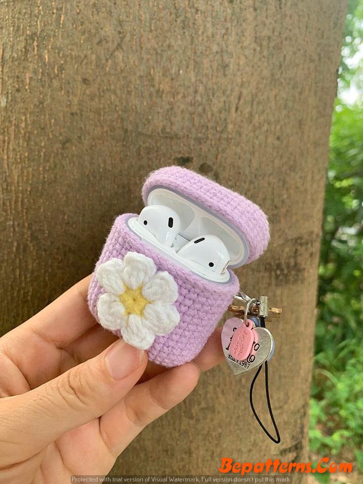 a hand holding an airpods case that has a flower on it and is attached to a tree