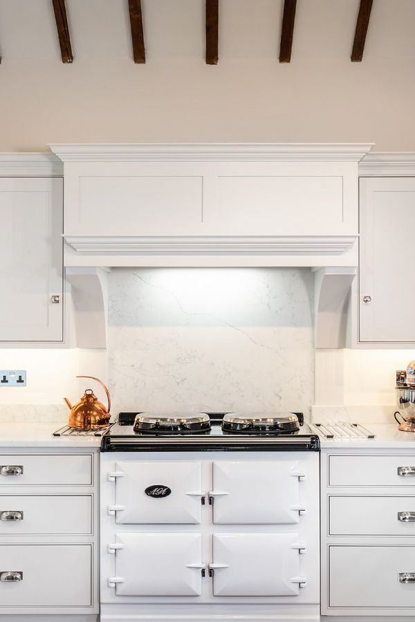 a white stove top oven sitting inside of a kitchen next to wooden ceiling beams and cabinets