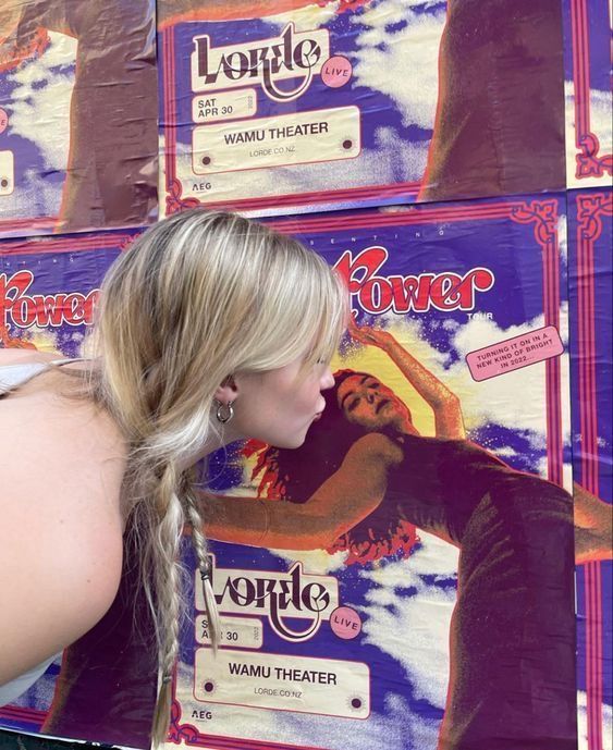 a woman leaning against a wall with posters on it's sides and her hair in a pony tail