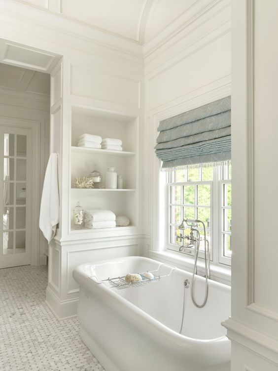 a white bath tub sitting under a window next to a shelf filled with towels and dishes