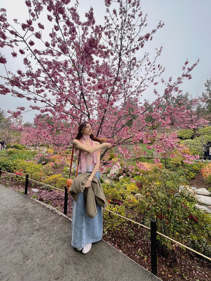 girl standing in front of Japanese cherry blossom tree wearing a spring outfit, pink top and denim skirt Cherry Blossom Fashion Outfit, Japanese Garden Outfit Ideas, Cherry Blossoms Outfit Ideas, Cherry Blossom Festival Outfit Ideas, Japan Spring Fashion Cherry Blossoms, Outfit For Cherry Blossom Season, Japan Outfit Cherry Blossom, Cherry Blossom Viewing Outfit, Japan Sakura Season Outfit