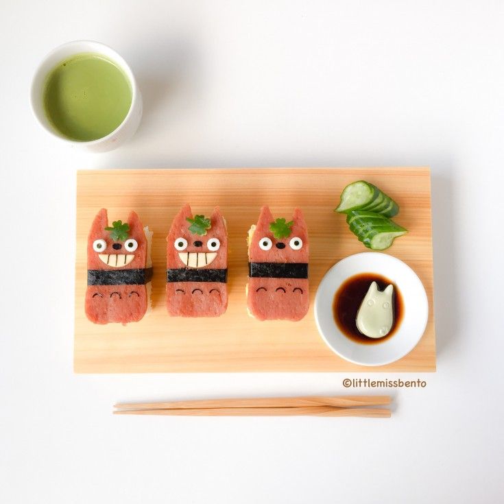 sushi with monster faces and chopsticks on a cutting board next to a cup of green tea