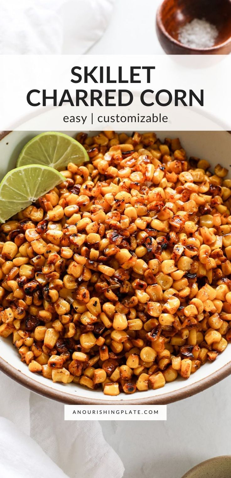 a bowl filled with roasted corn next to a lime wedge and some sauce on the side