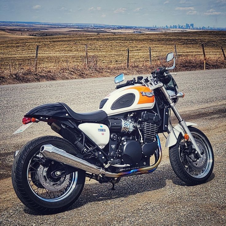 an orange and white motorcycle parked on the side of the road next to a fence