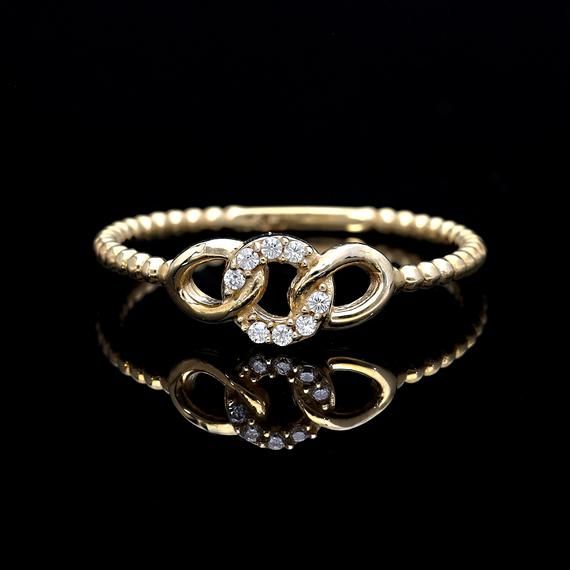 a gold ring with two intertwined hearts and white diamonds on the side, against a black background