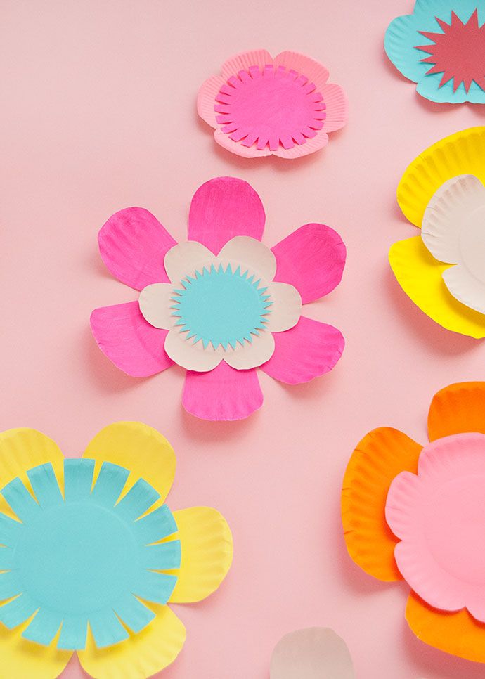 paper plates with flowers cut out of them sitting on a pink surface, ready to be used as decorations