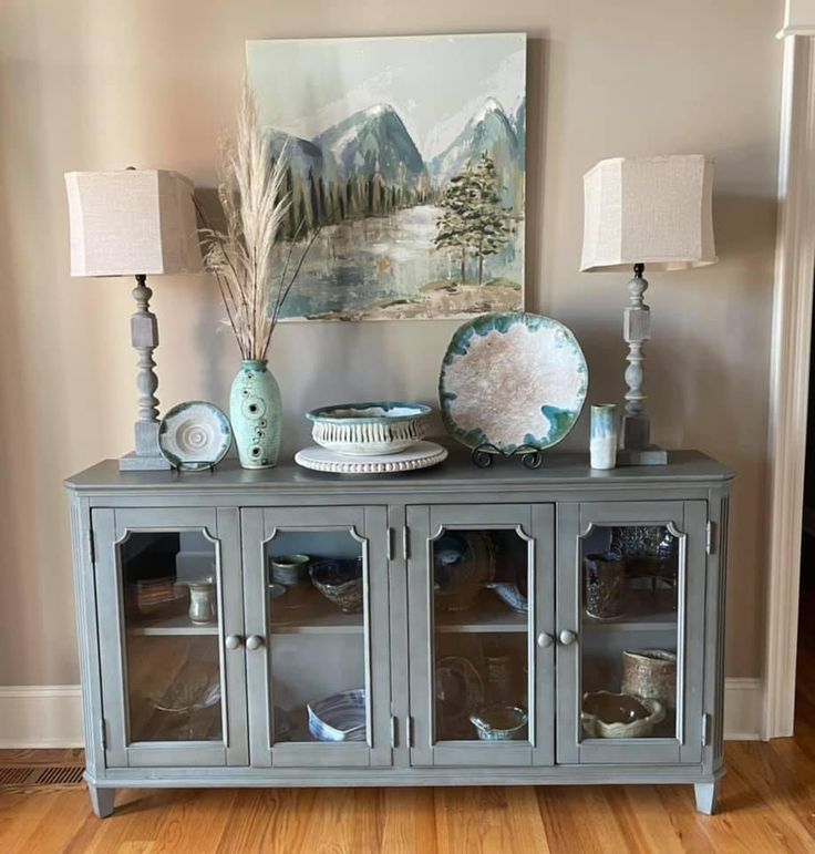 a blue and white china cabinet with two lamps on it's sides, in front of a painting