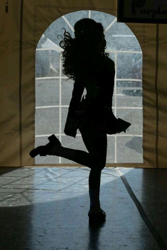 the silhouette of a woman dancing in front of a window with her legs spread out