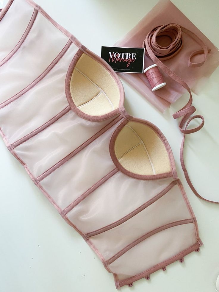 a pair of pink bras with ribbon and sewing thread on the table next to it