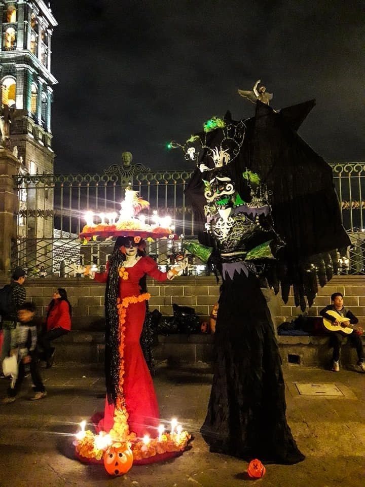 two people dressed up in costumes with candles on the ground near a clock tower at night