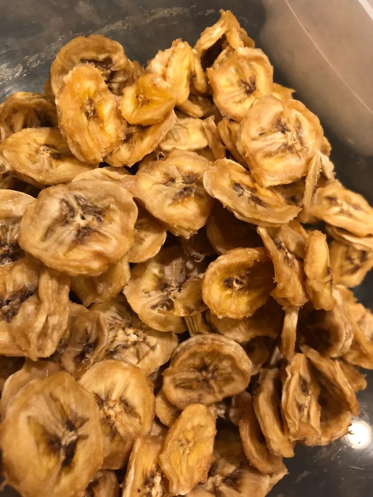 a pile of dried bananas sitting on top of a metal bowl next to a spoon