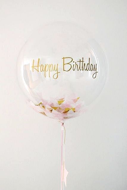 a clear balloon filled with pink flowers and the words happy birthday in gold foil lettering