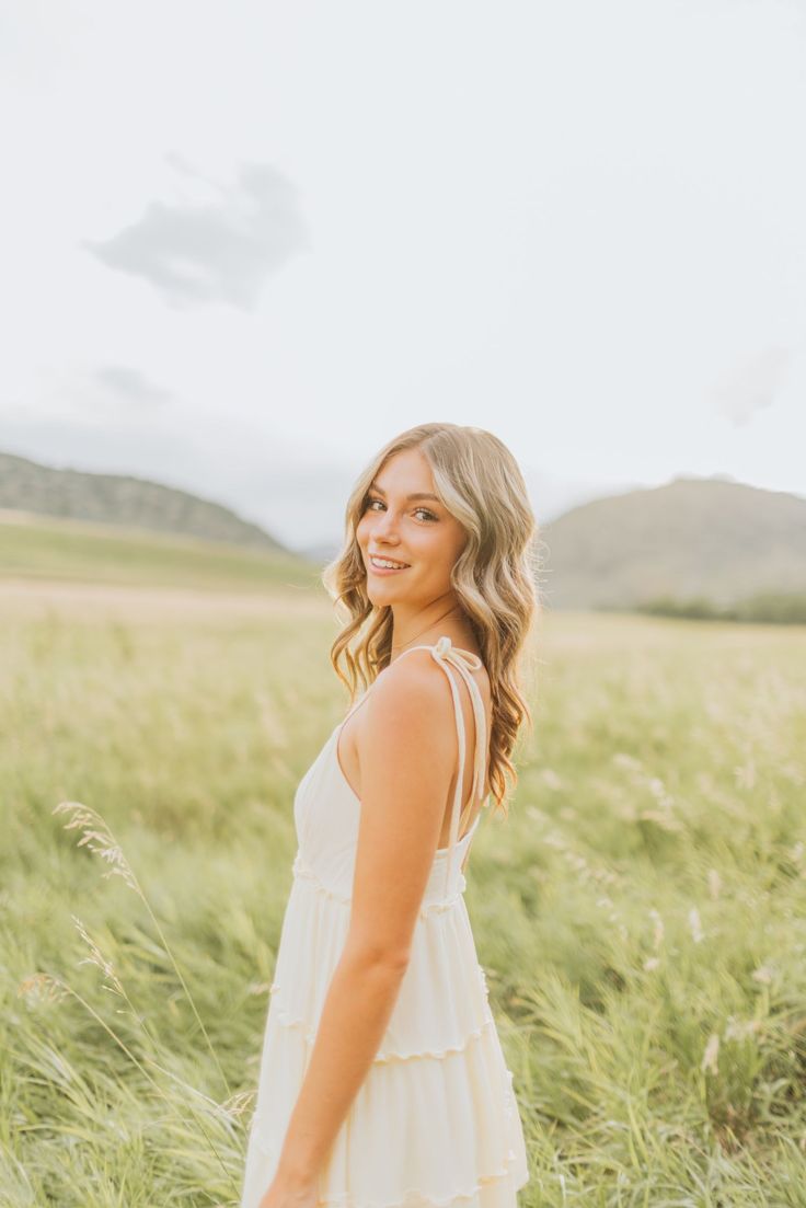 a woman standing in the middle of a field with tall grass and mountains in the background