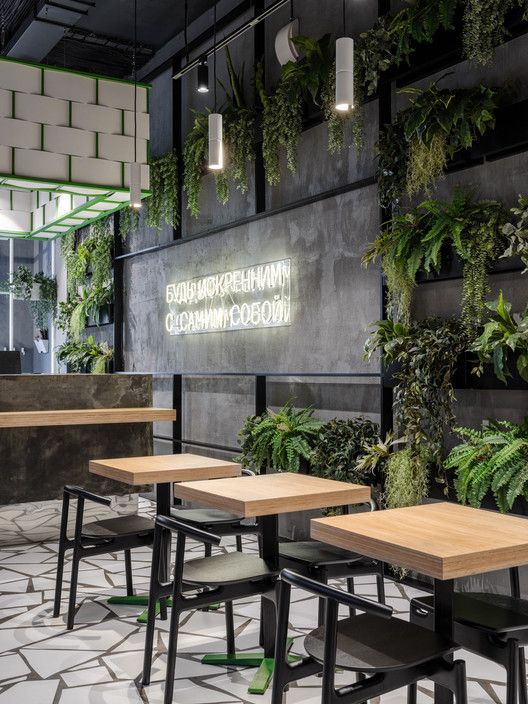 the interior of a restaurant with plants growing on the wall and tables in front of it