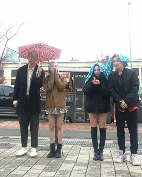 four people standing on the sidewalk with umbrellas over their heads and one woman holding an umbrella