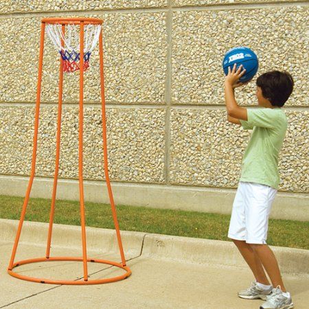 a young boy holding a blue basketball in front of an orange hoop on the sidewalk