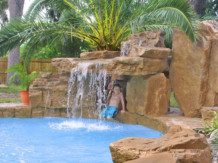 a boy is playing in the pool next to a waterfall