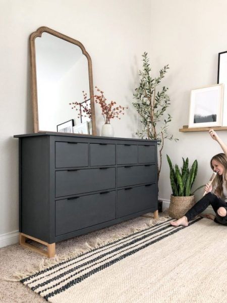 a woman is sitting on the floor in front of a dresser and mirror with plants