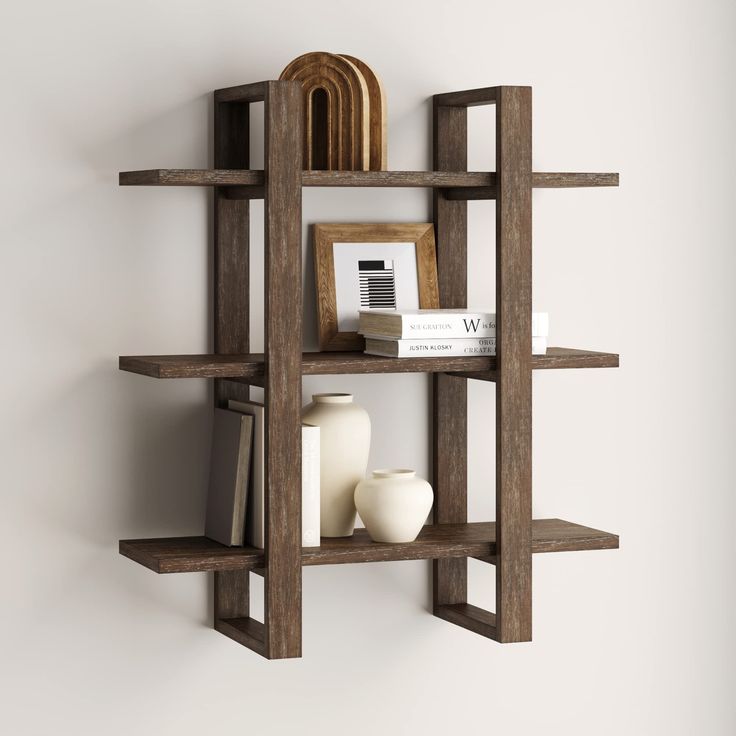 a wooden shelf with books, vases and other items on it against a white wall