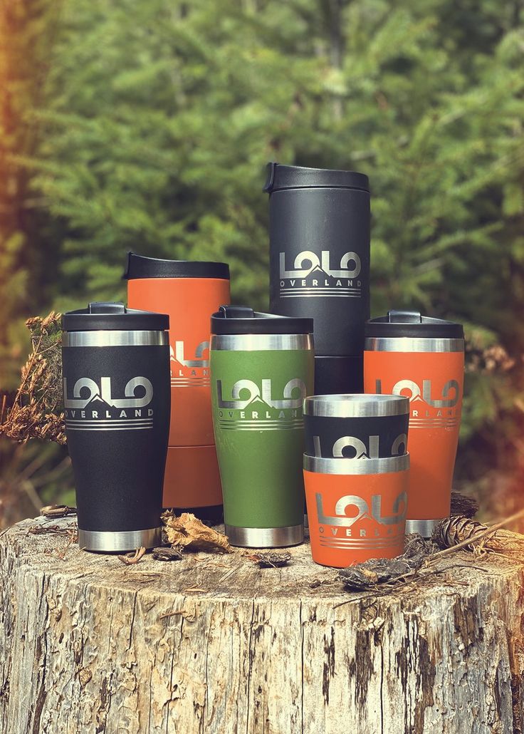 six travel mugs sitting on top of a tree stump in front of some trees