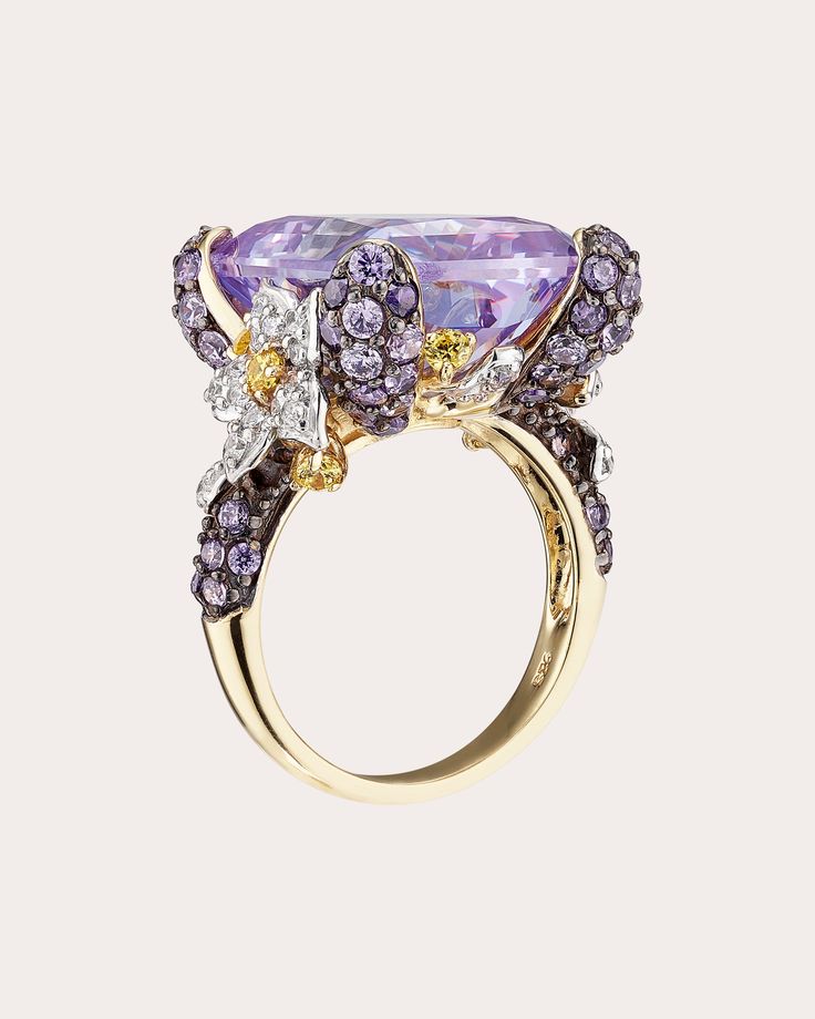 a gold ring with purple and white stones on the front, surrounded by other jewels