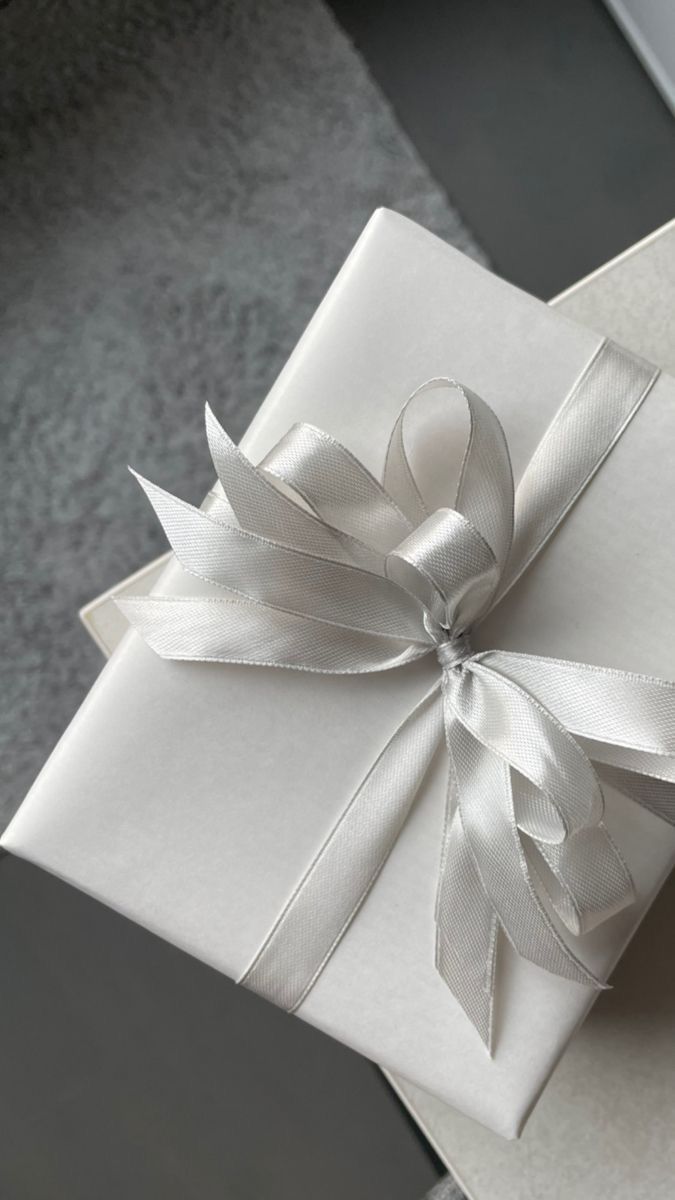 a white gift box with a ribbon on it's side and a bow around the top