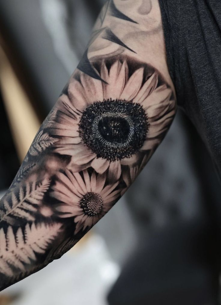 a man's arm with sunflowers and leaves tattooed on the arm, in black and white