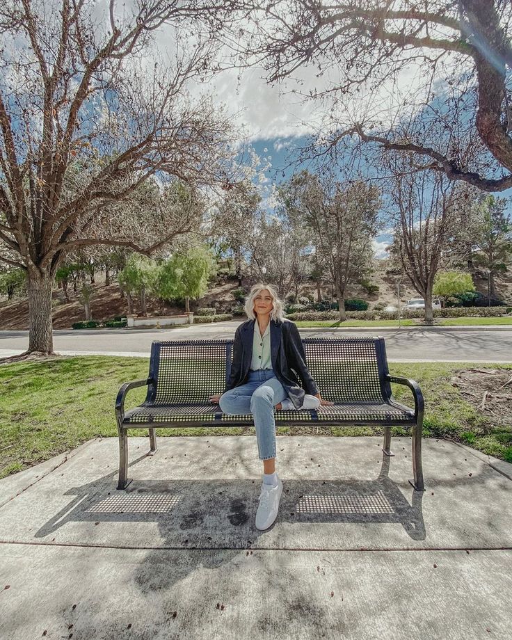 a woman sitting on top of a metal bench in the middle of a park next to trees