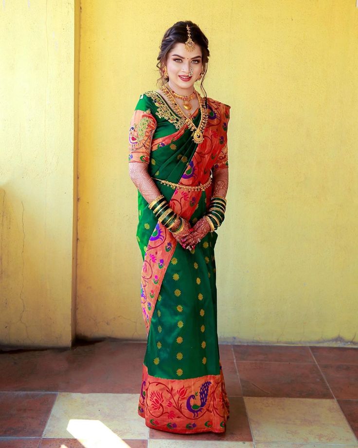 a woman in a green and red sari standing on a tile floor next to a yellow wall