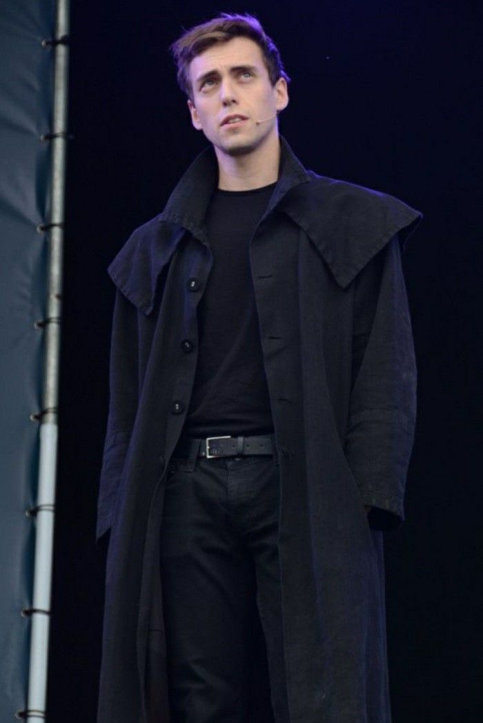 a man standing in front of a stage wearing a black coat