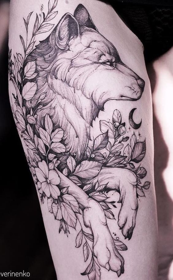 a woman's thigh with a wolf and flowers tattoo design on her leg,