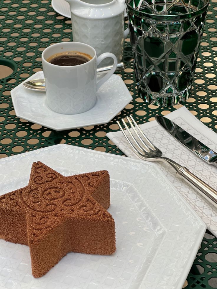 a star shaped cookie sitting on top of a white plate next to a cup of coffee