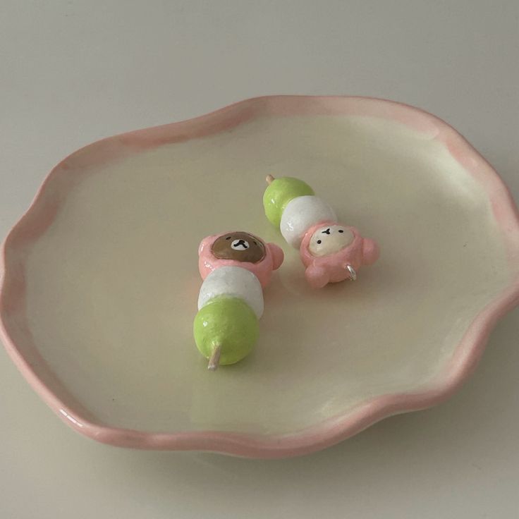 two small toy animals sitting on top of a pink and white plate with green handles