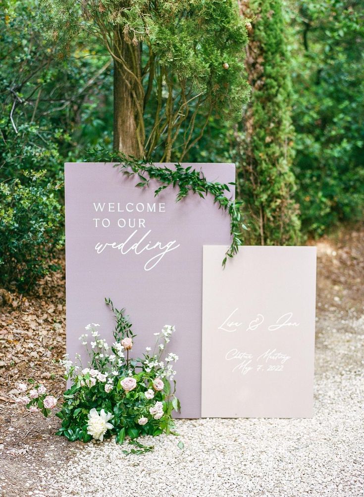 a welcome sign with flowers and greenery on the ground in front of some trees