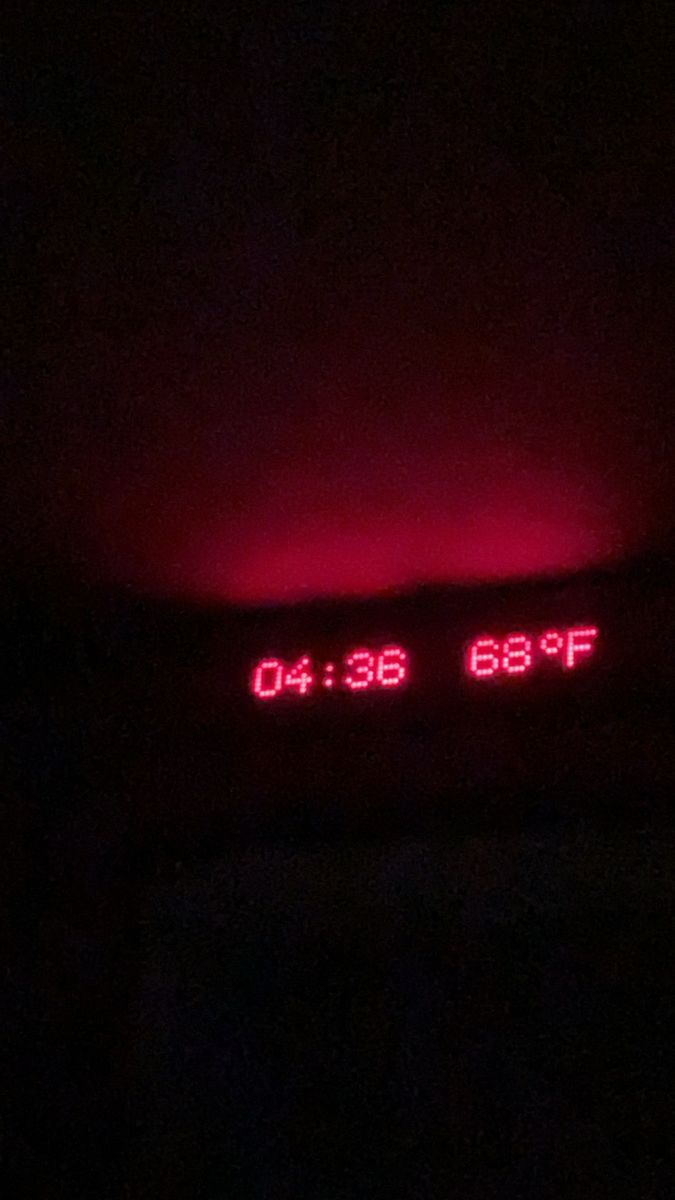 the clock is lit up in the dark with red light on it's side