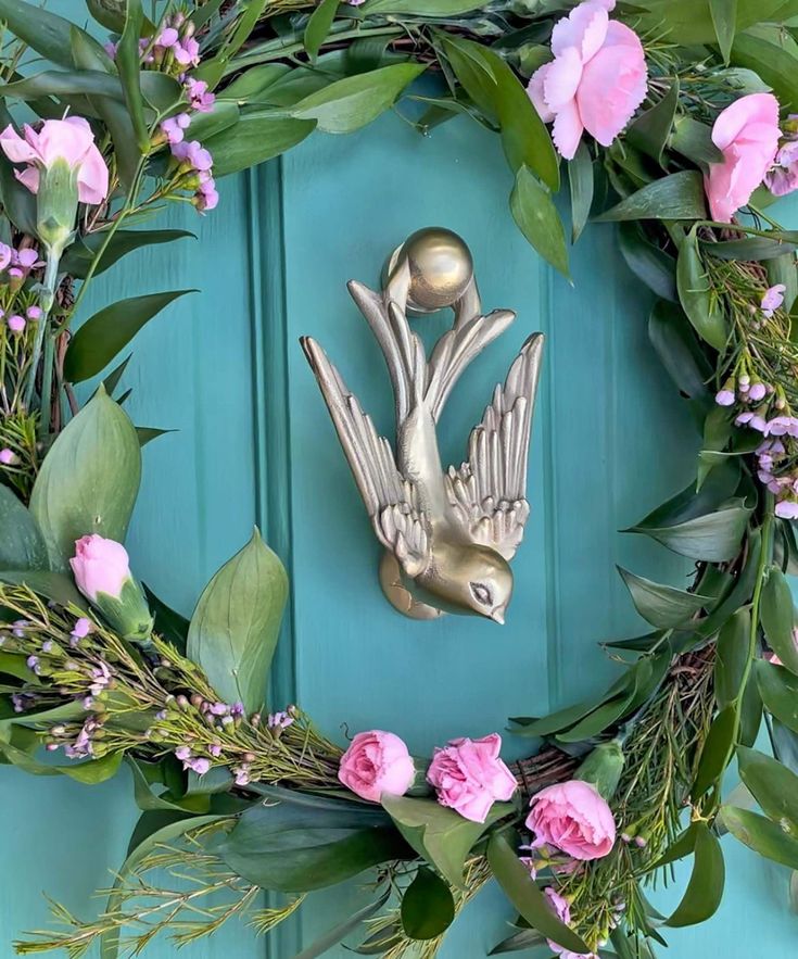 a wreath with pink flowers and green leaves on the front door is adorned with a metal bird ornament