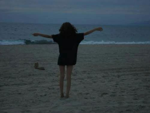 a woman standing on top of a sandy beach next to the ocean under a cloudy sky