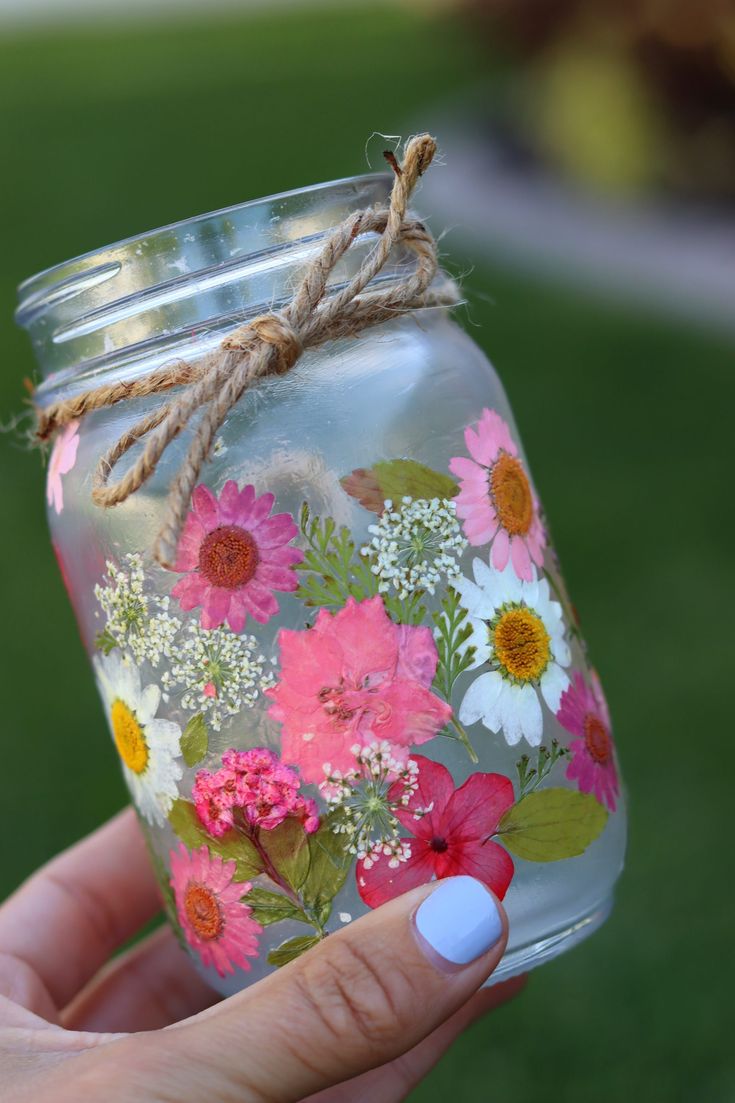 a hand holding a mason jar with flowers painted on the inside and string tied to it