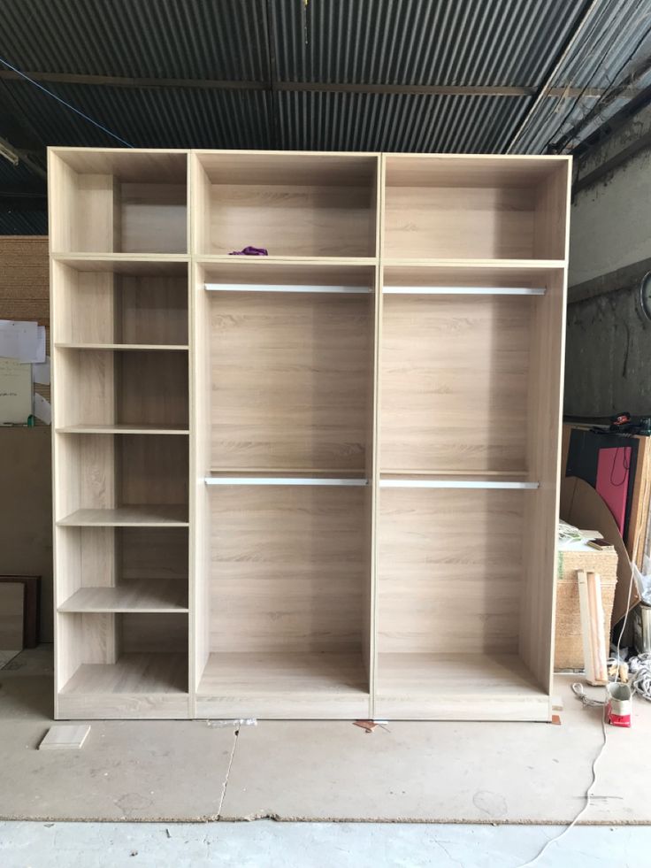 an unfinished bookcase in a garage with no doors or drawers on the shelves and one door open