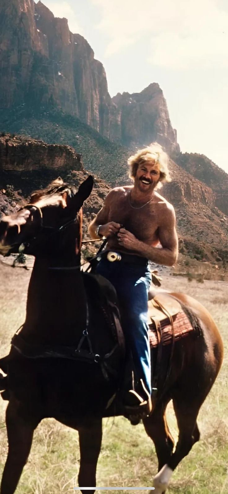 a shirtless man riding on the back of a brown horse in front of mountains