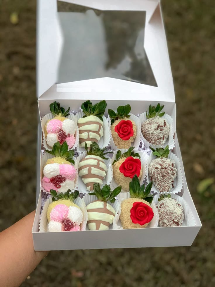 a hand holding a box filled with assorted chocolate covered strawberries and pastries