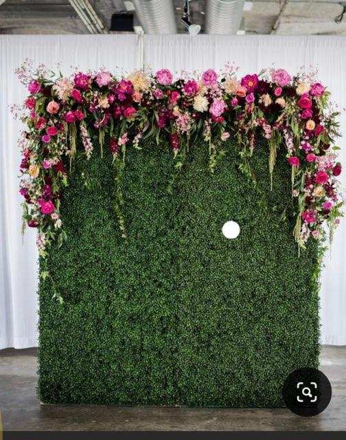 an artificial wall with flowers and greenery on it in front of a white backdrop