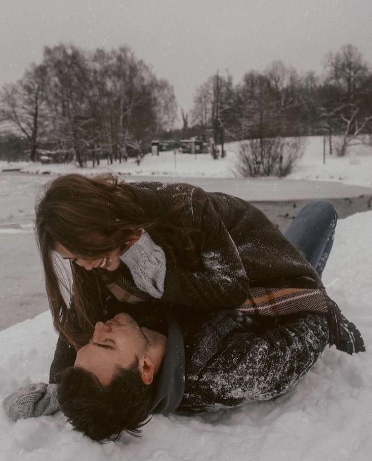 a man and woman laying in the snow with their heads touching each other's foreheads