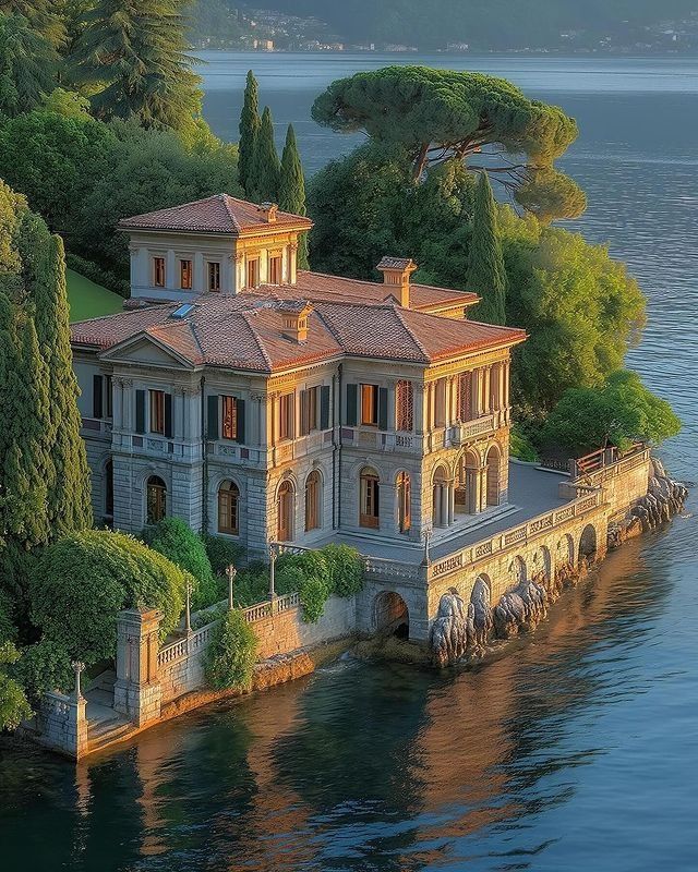 an aerial view of a house on the water with trees around it and mountains in the background