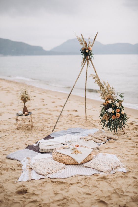 an outdoor picnic setting on the beach with flowers and blankets laid out in front of it