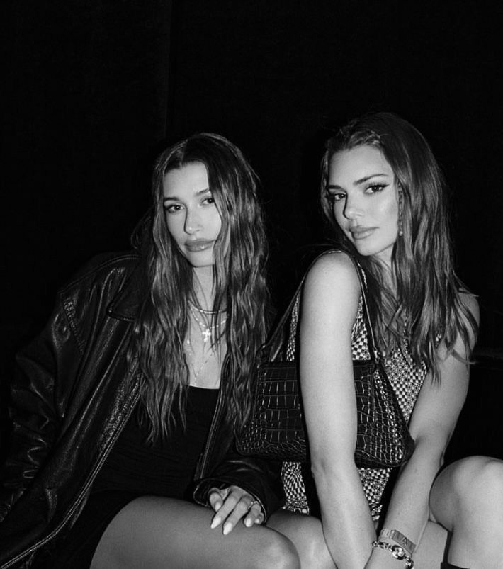 two beautiful young women sitting next to each other in black and white photo with one woman's legs crossed