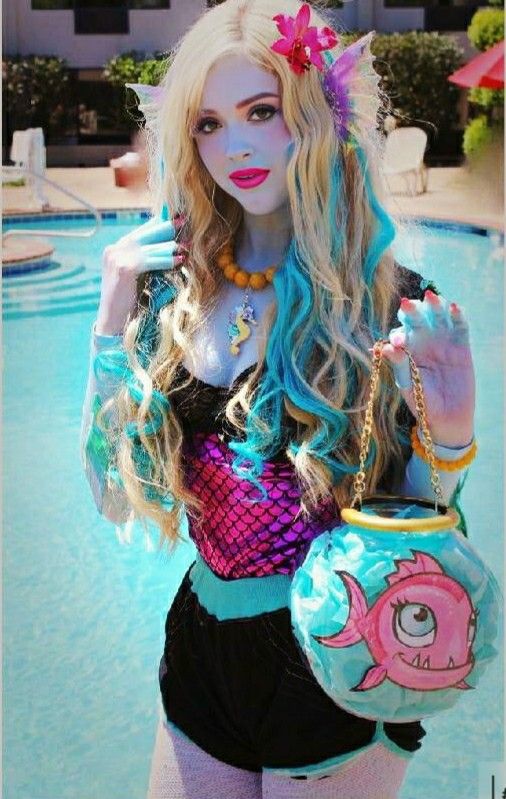 a woman dressed as a mermaid holding a purse in front of a swimming pool with a pink fish on it