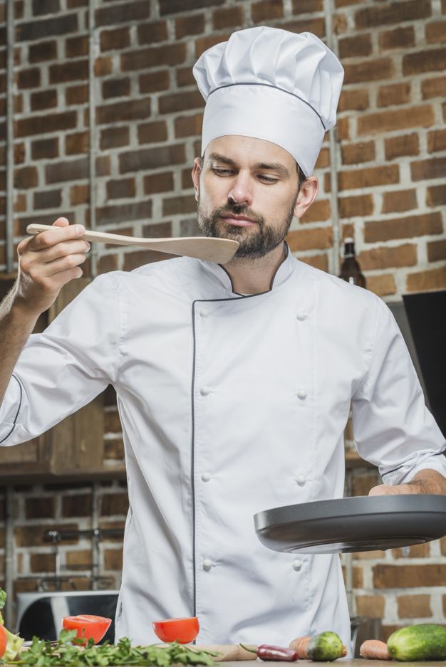 a man in a chef's outfit is holding a spoon over his mouth as he cooks